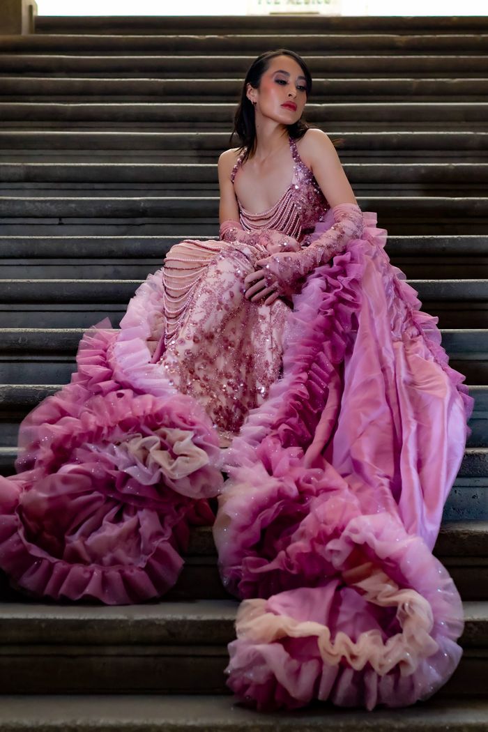 Sophisticated woman wearing a glamorous pink gown, sitting gracefully on stairs.