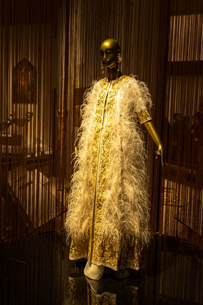 ours-journey Golden mannequin showcasing elegant feathered gown in a dim-lit boutique setting.